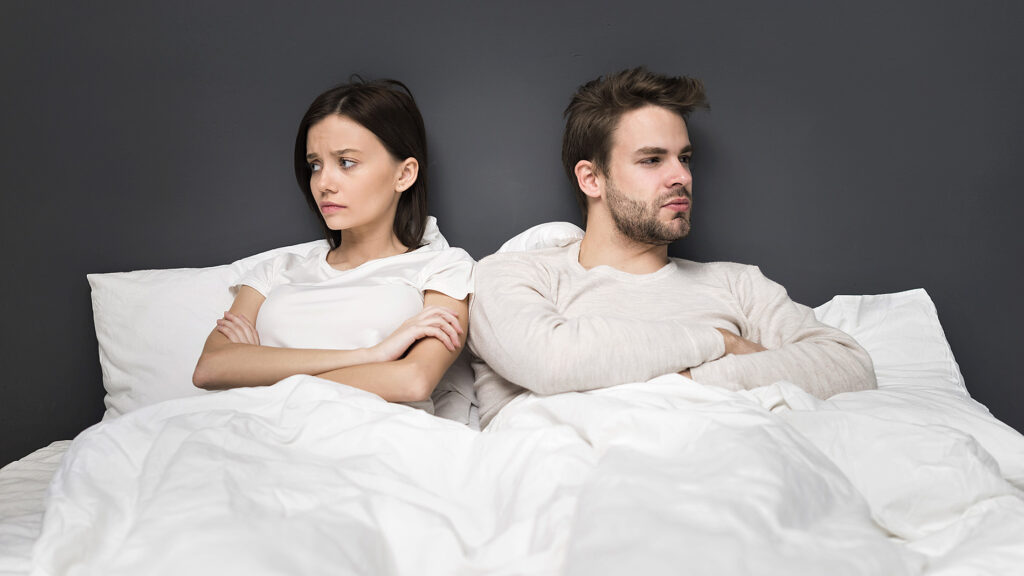 Paar sitzt im Bett und schaut genervt in unterschiedliche Richtungen