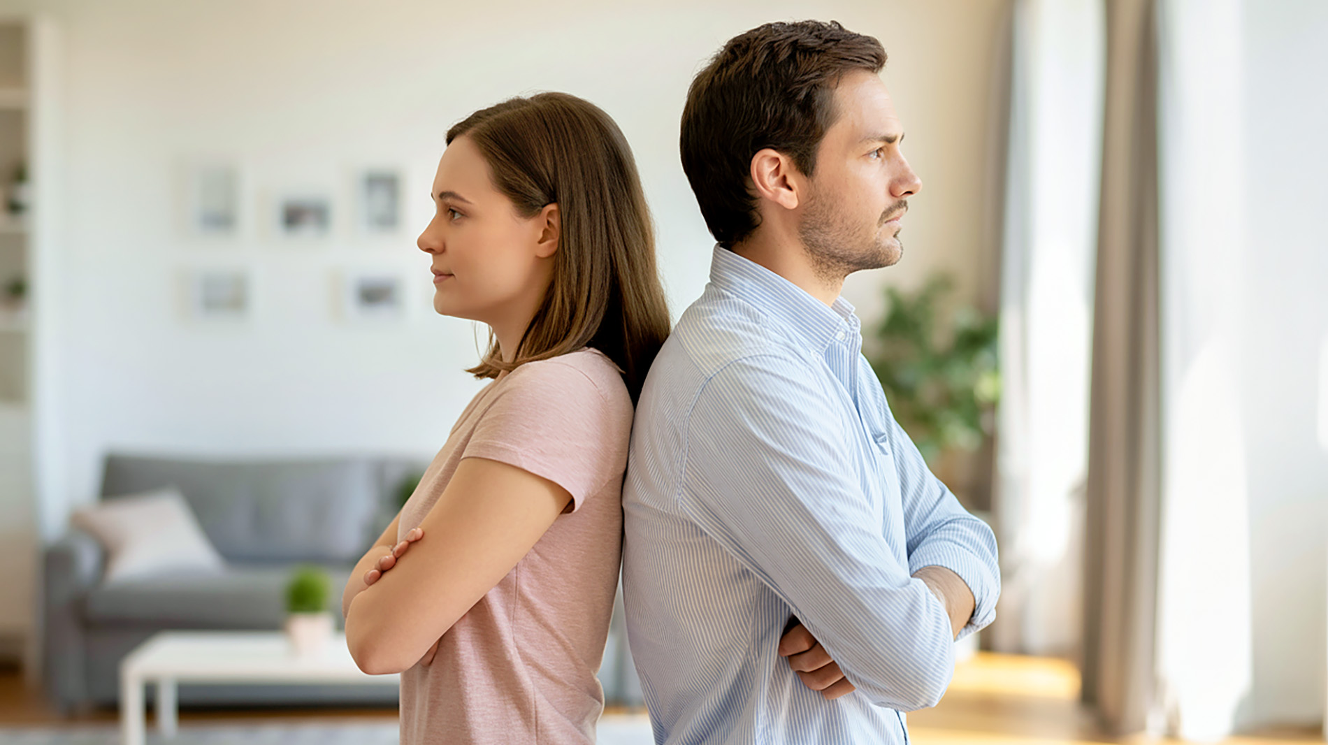 Ein Paar steht Rücken an Rücken in einer Wohnung, beide blicken in entgegengesetzte Richtungen. Das Bild symbolisiert fehlendes Teamgefühl und emotionale Distanz.