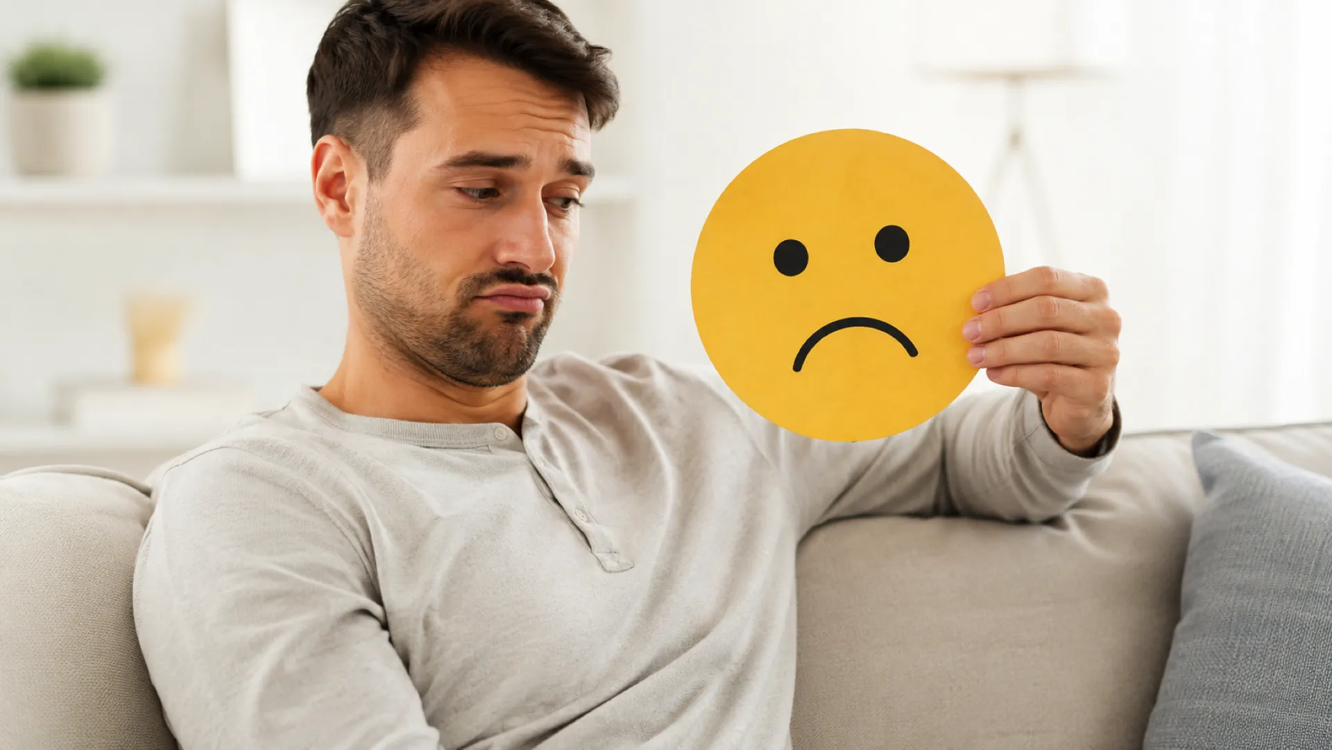 Mann hält ein trauriges Symbol als Sinnbild für Erektionsprobleme und seelischen Druck